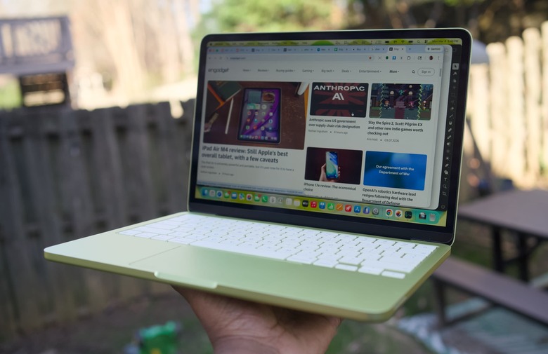 A citrus MacBook Neo being held up with one hand.