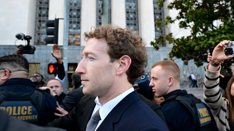 Profile view of Mark Zuckerberg, surrounded by police, outside a courthouse